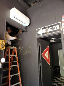 A technician standing on a ladder working on an air conditioner.